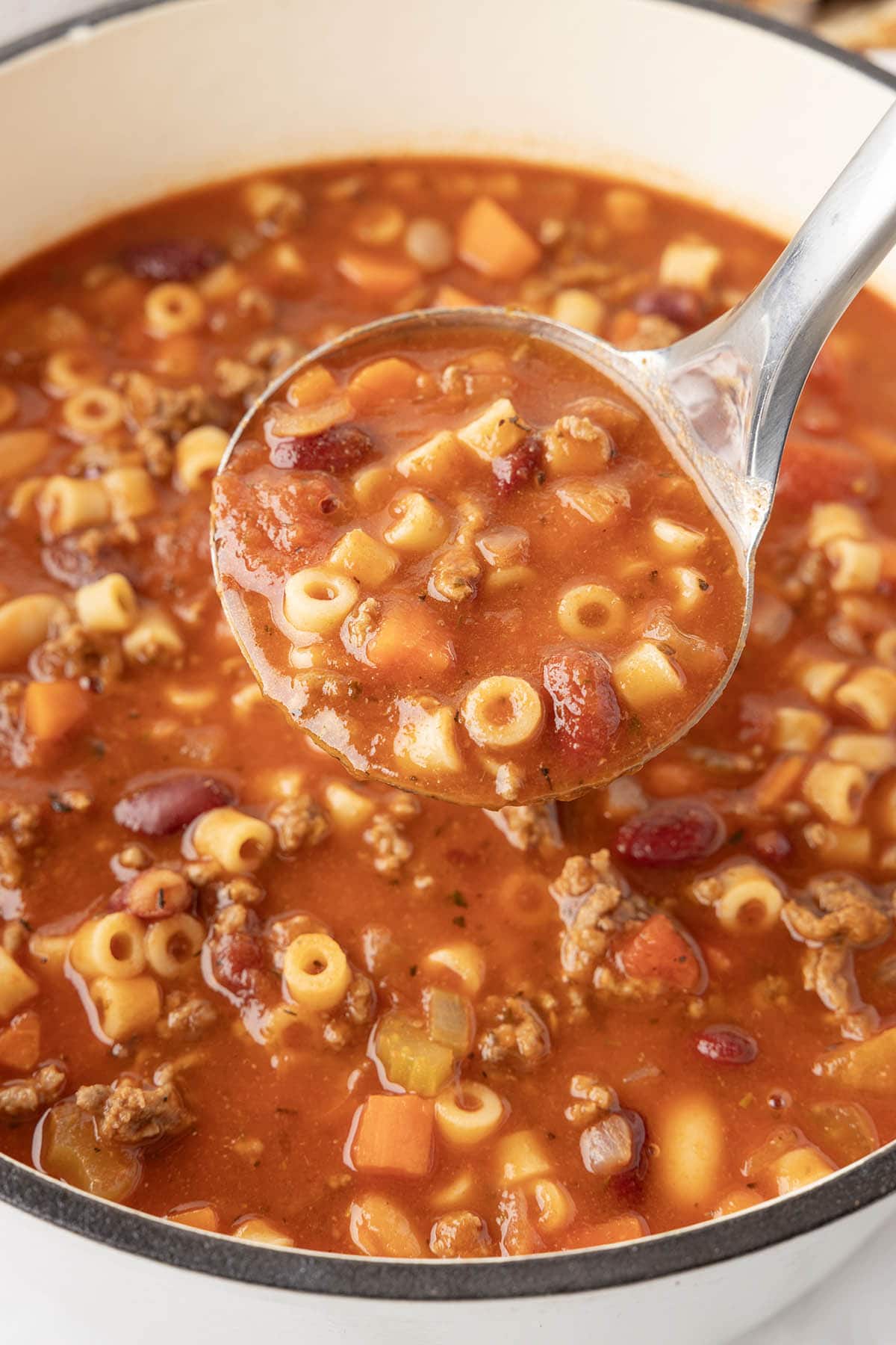 Ladle scooping hearty pasta e fagioli soup with ditalini pasta, beans, ground beef, and veggies in tomato broth.
