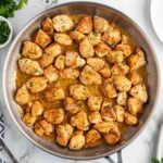 Skillet filled with golden brown garlic butter chicken bites, garnished with chopped parsley and simmering in a savory sauce.