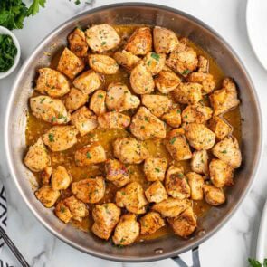 Skillet filled with golden brown garlic butter chicken bites, garnished with chopped parsley and simmering in a savory sauce.