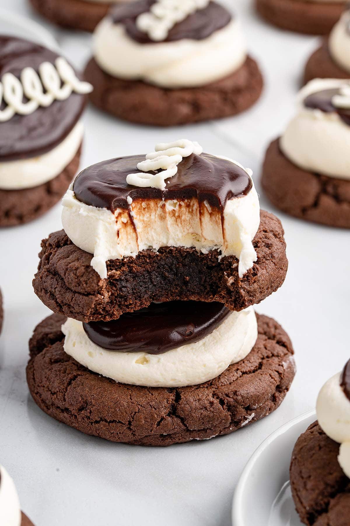 A stack of Hostess-inspired cupcake cookies, with the top cookie showing a rich chocolate bite revealing fluffy cream and moist chocolate cookie layers.
