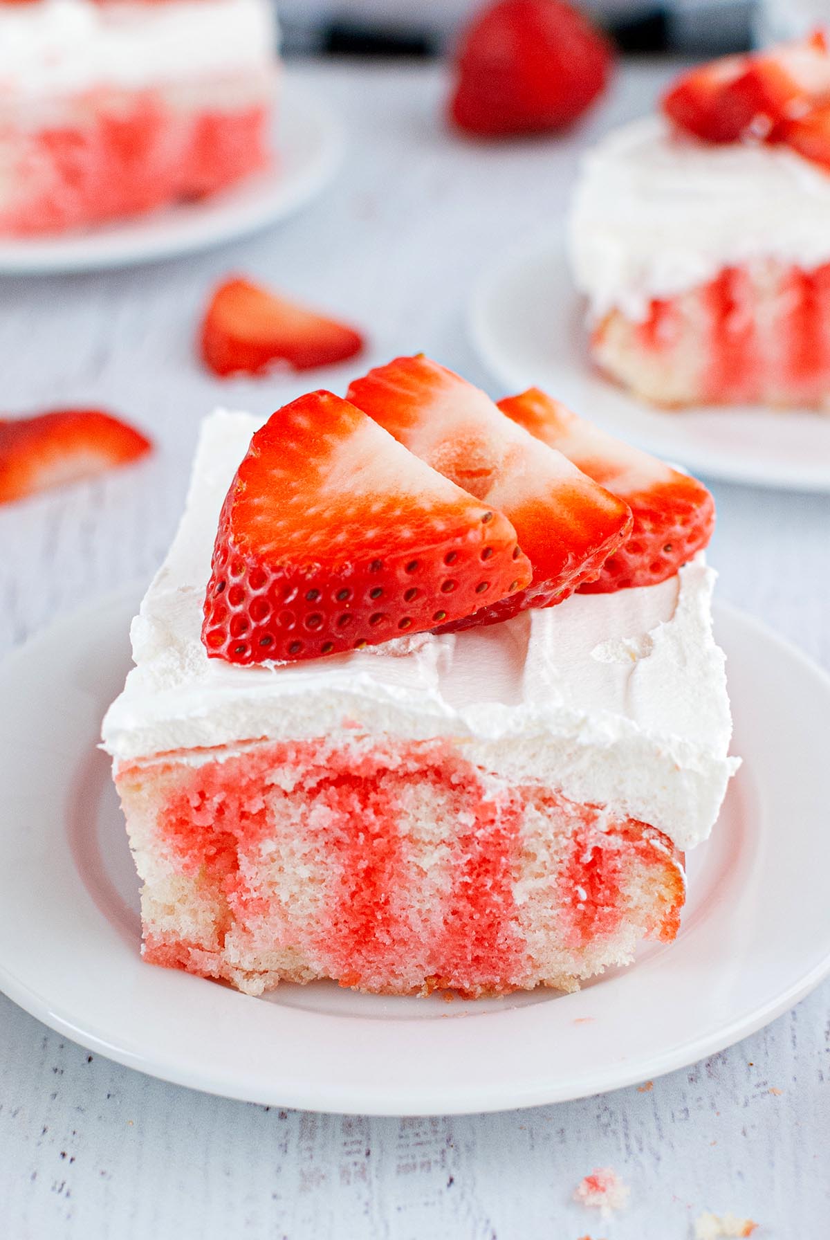 Piece of strawberry jello poke cake with three fresh strawberries on top.