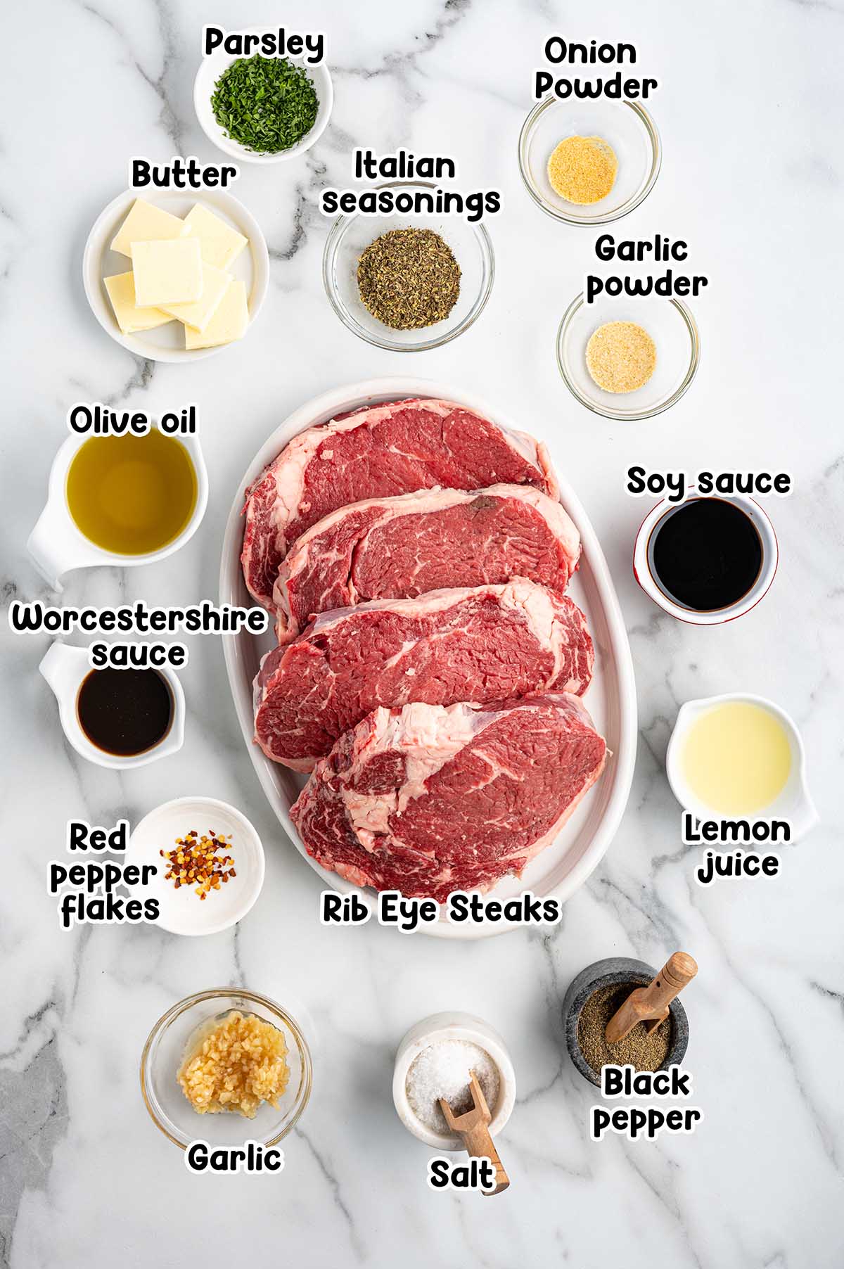 flatlay of steak marinade ingredients including rib eye steak, worchestershire sauce, olive oil, garlic powder, lemon juice.