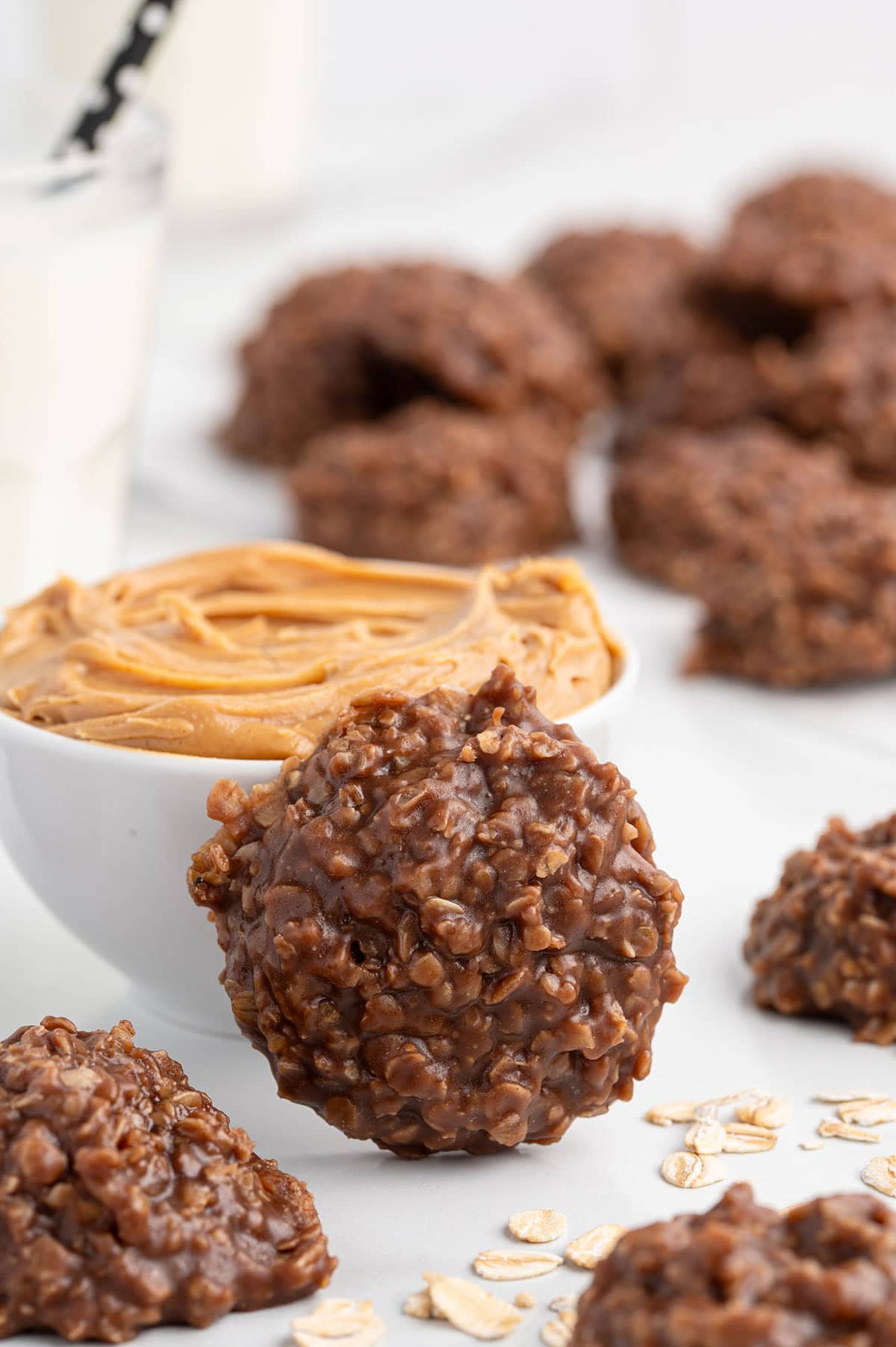 Chocolate peanut butter no bake cookies arranged near a bowl of creamy peanut butter.