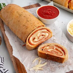 a loaf of pepperoni roll cut into 2 slices on top of wooden board.