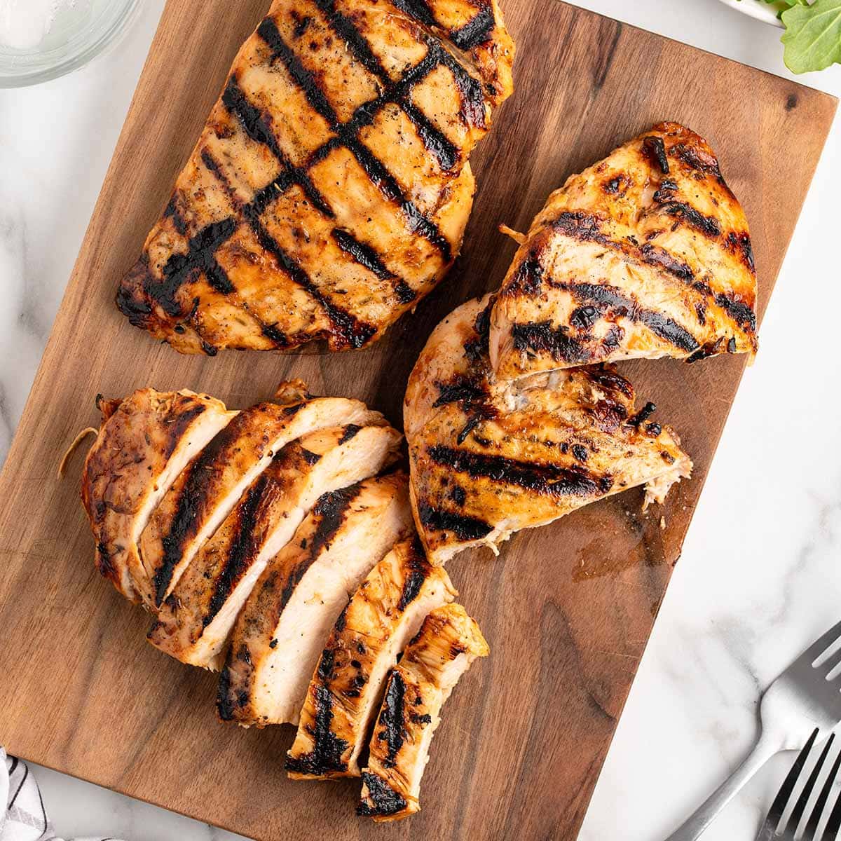 Juicy grilled chicken breast with clear char marks on a wooden cutting board.
