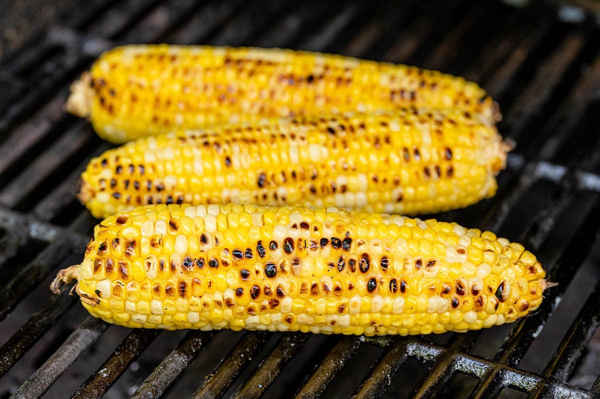 Fresh corn on the cob cooking over hot grill grates.