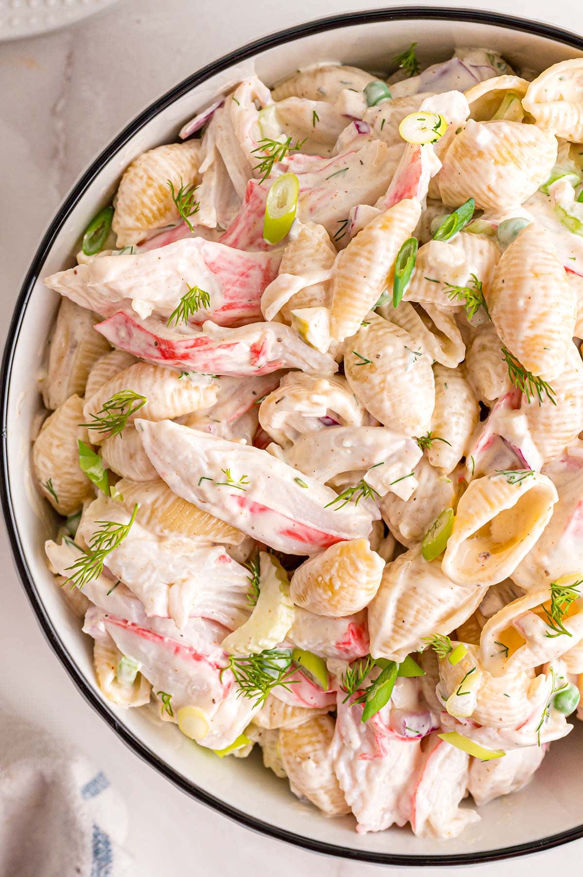 A bowl filled with creamy pasta salad mixed with crab and garnished with dill.