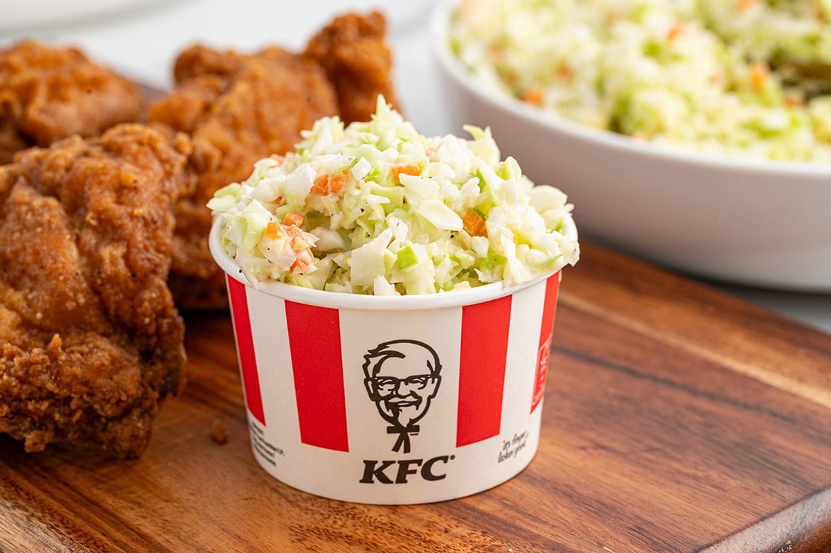 A cup of creamy KFC-style coleslaw on a wooden board.