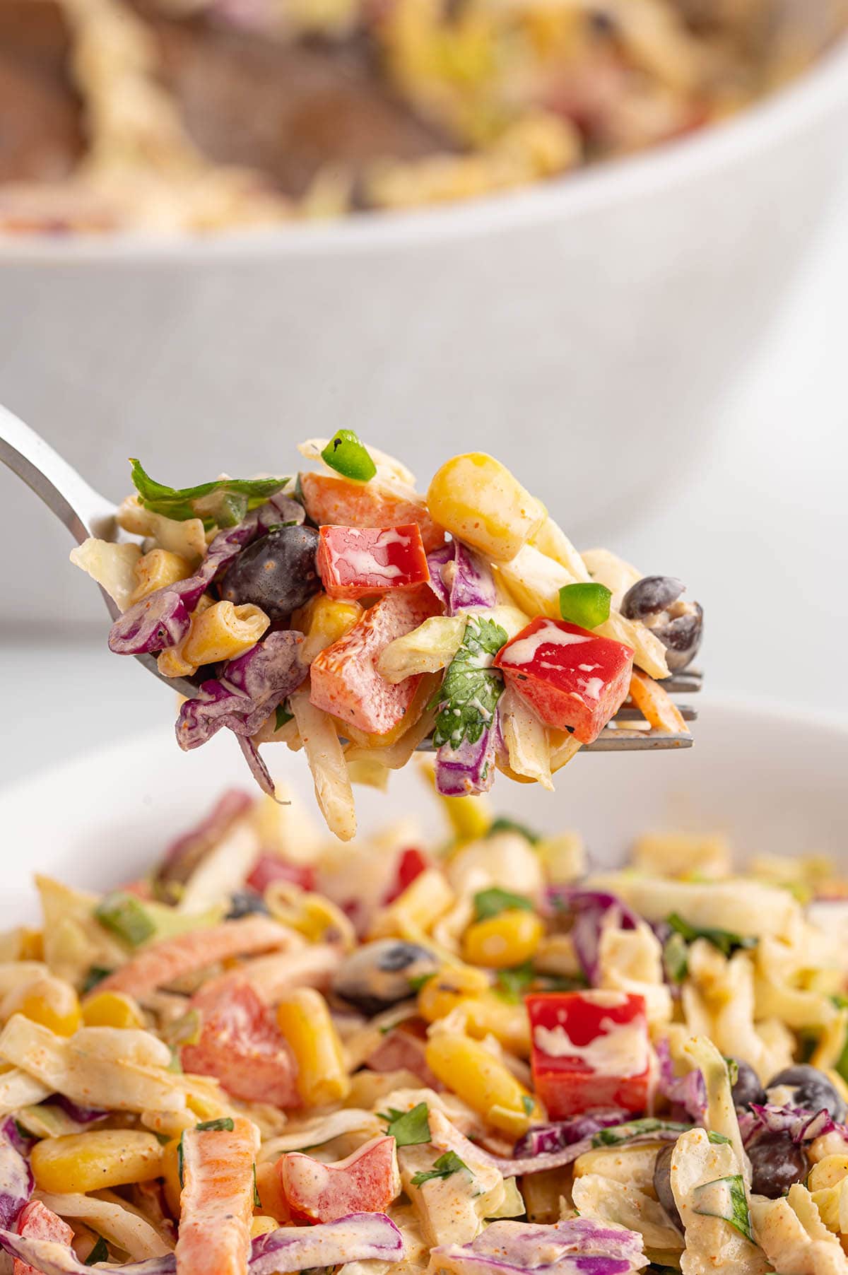 A close-up of Mexican coleslaw with colorful veggies and creamy dressing on a fork.