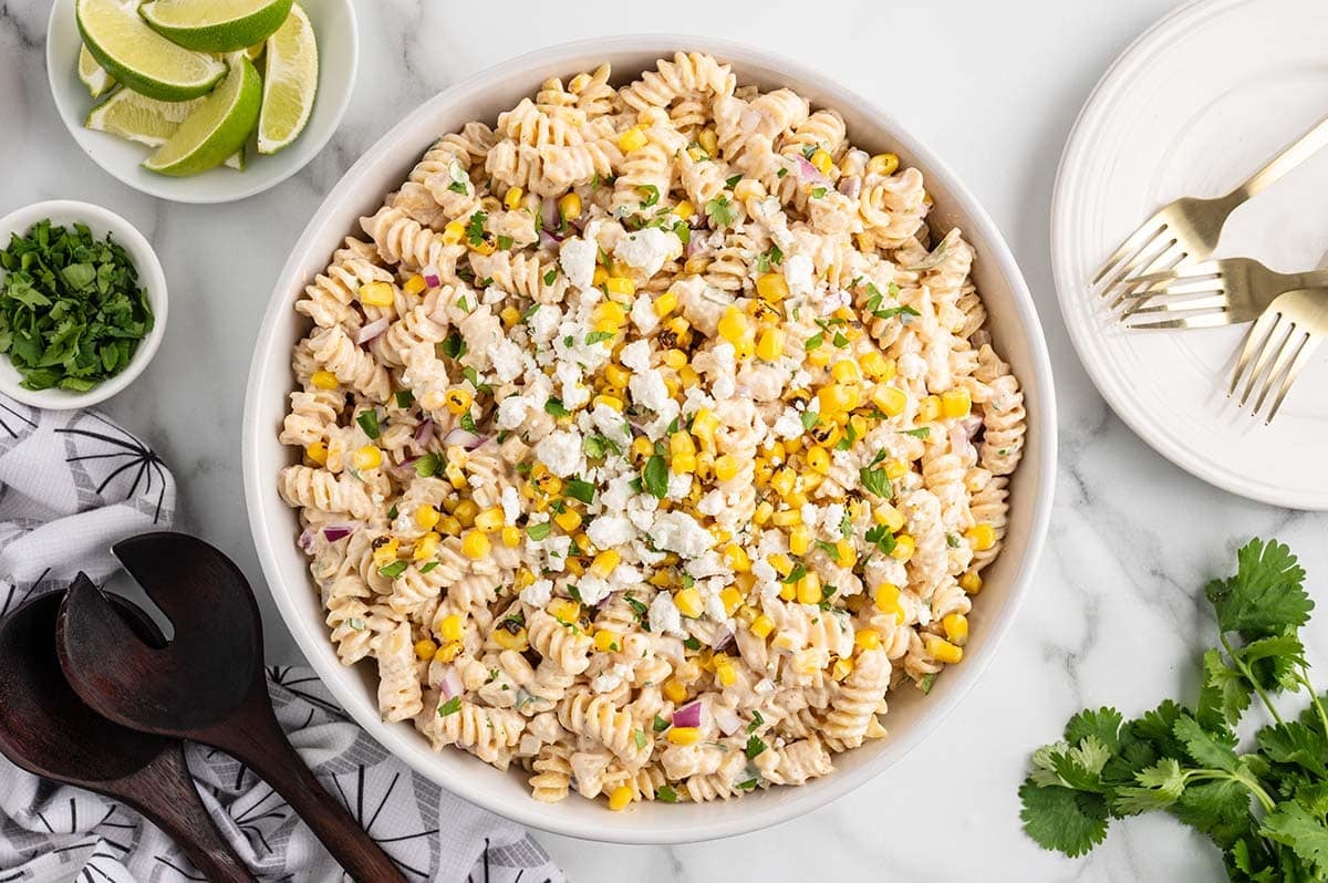 A bowl full of creamy street corn pasta salad garnished with fresh herbs and crumbled cheese.