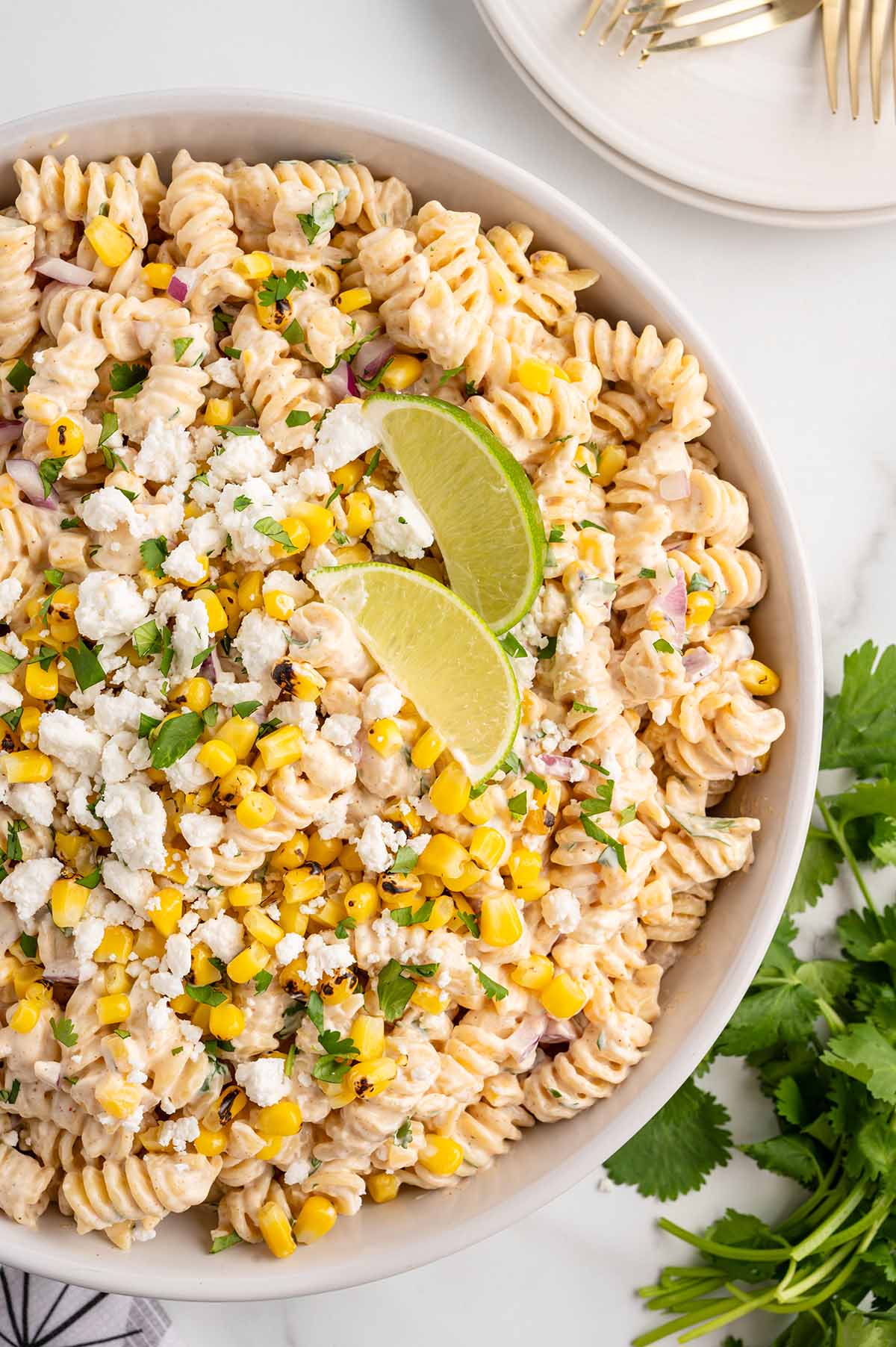 Fresh pasta salad with grilled corn kernels, red onion bits, and two lime wedges on top.