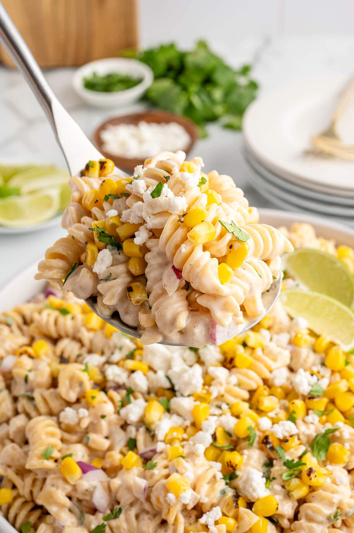 A spoonful of street corn pasta salad with lime wedges in the background.
