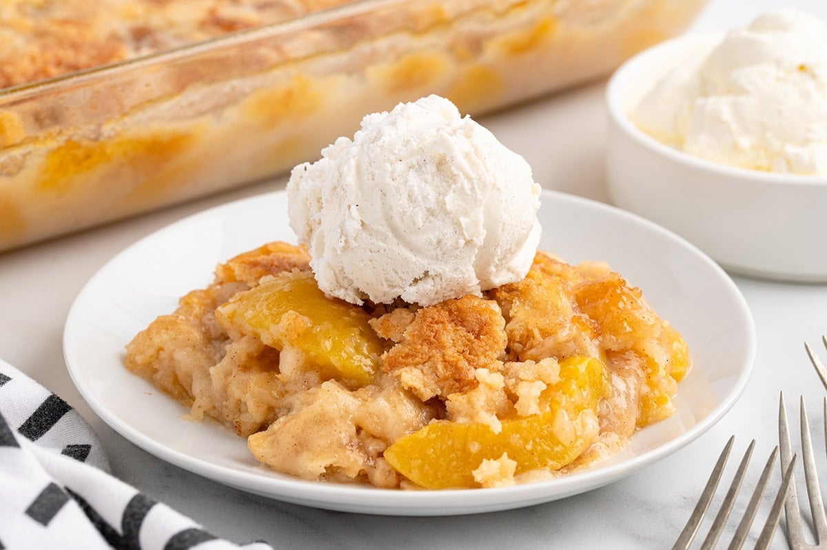 A warm peach dump cake topped with a scoop of vanilla ice cream on a white plate.