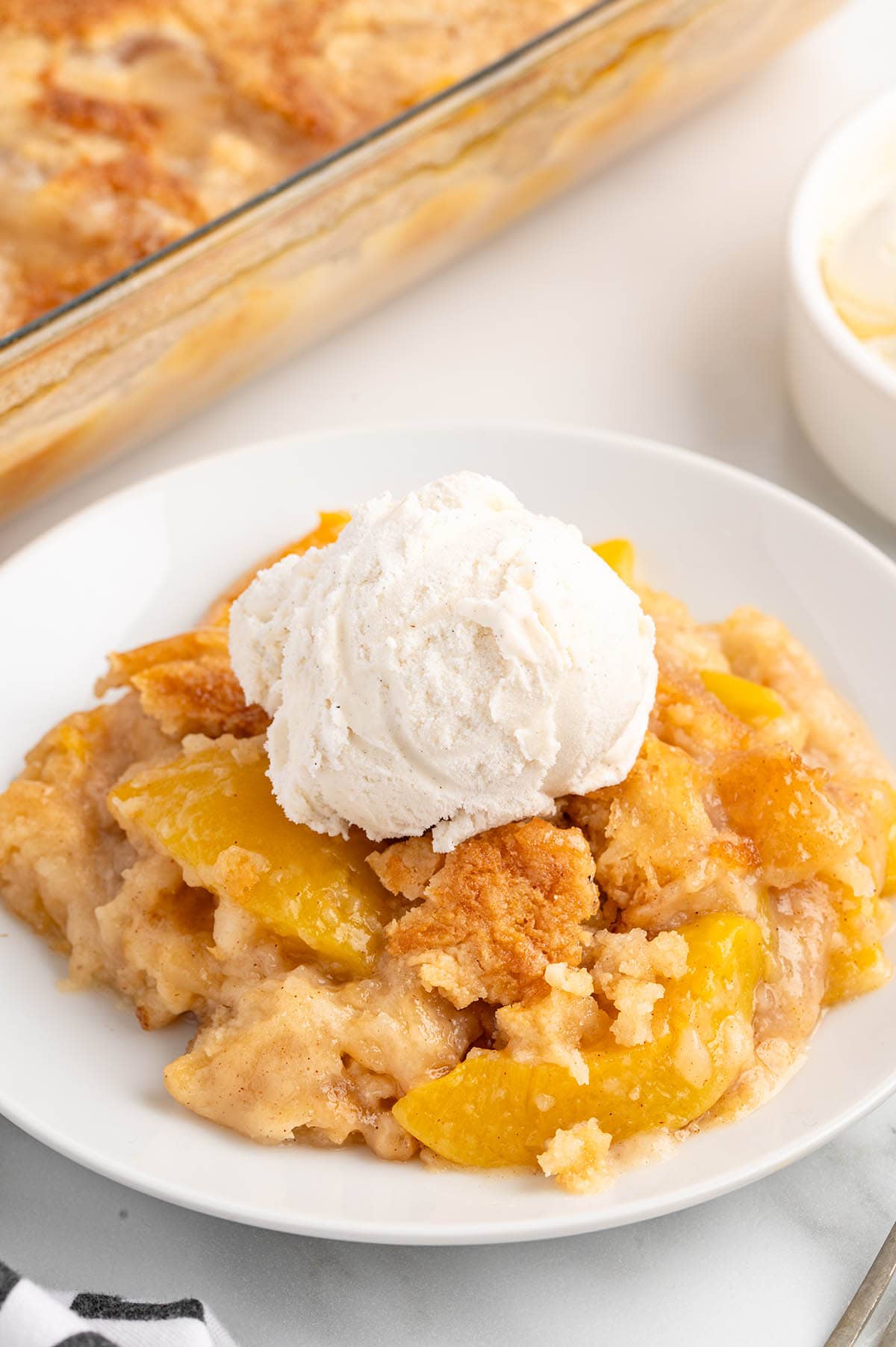 peach dump cake served on a white plate with a scoop of vanilla ice cream on top.