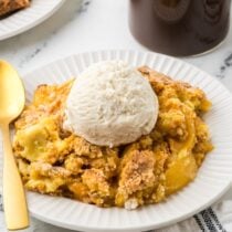 A plate with warm peach cobbler topped with a scoop of vanilla ice cream.