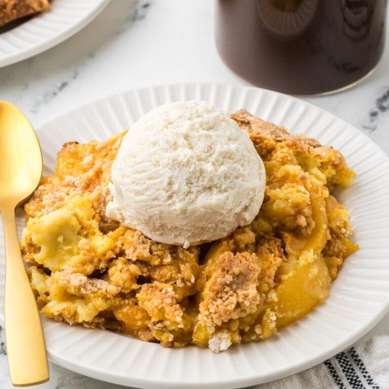 A plate with warm peach cobbler topped with a scoop of vanilla ice cream.