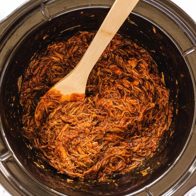 Slow-cooked BBQ pulled chicken in a crockpot with a wooden spoon.