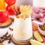 Glass of apple cider float garnished with cinnamon and star anise on a wooden coaster.