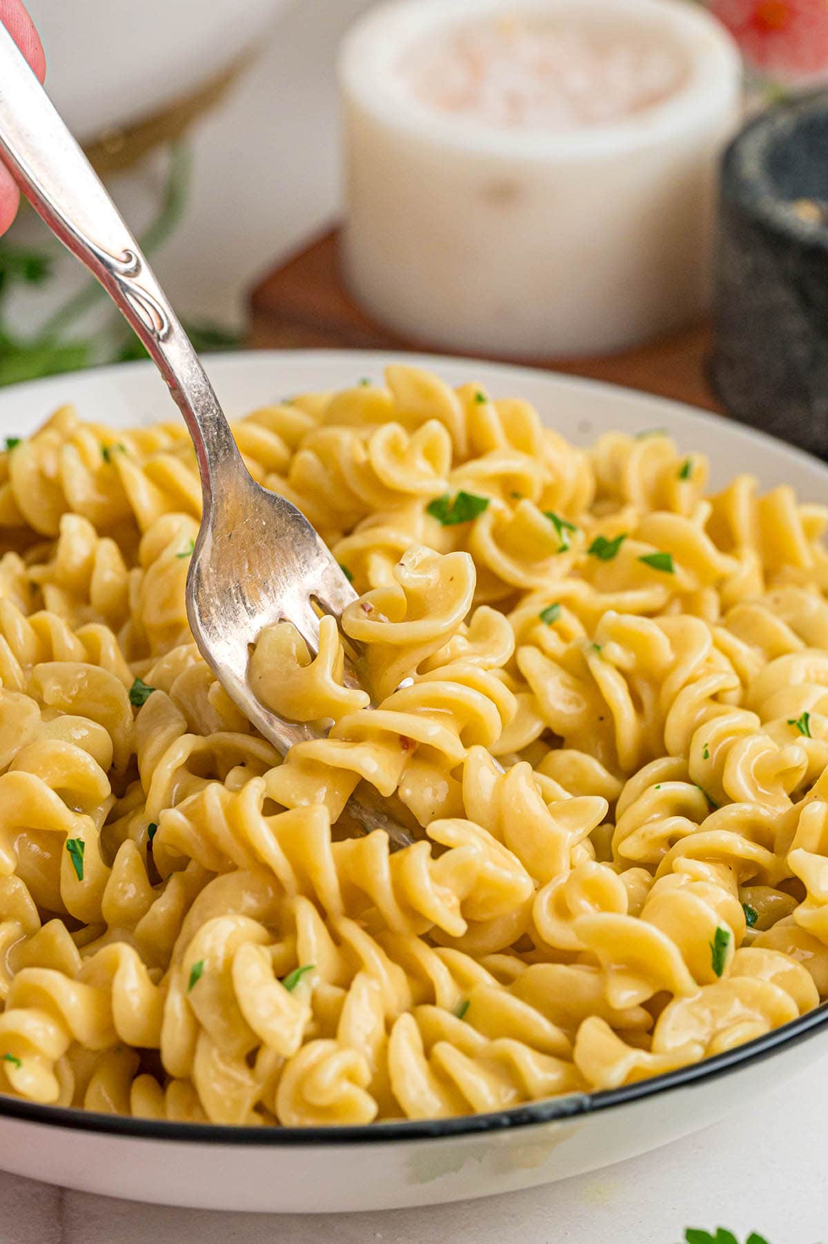 Fork lifting a bite of cheesy spiral pasta from a white bowl.