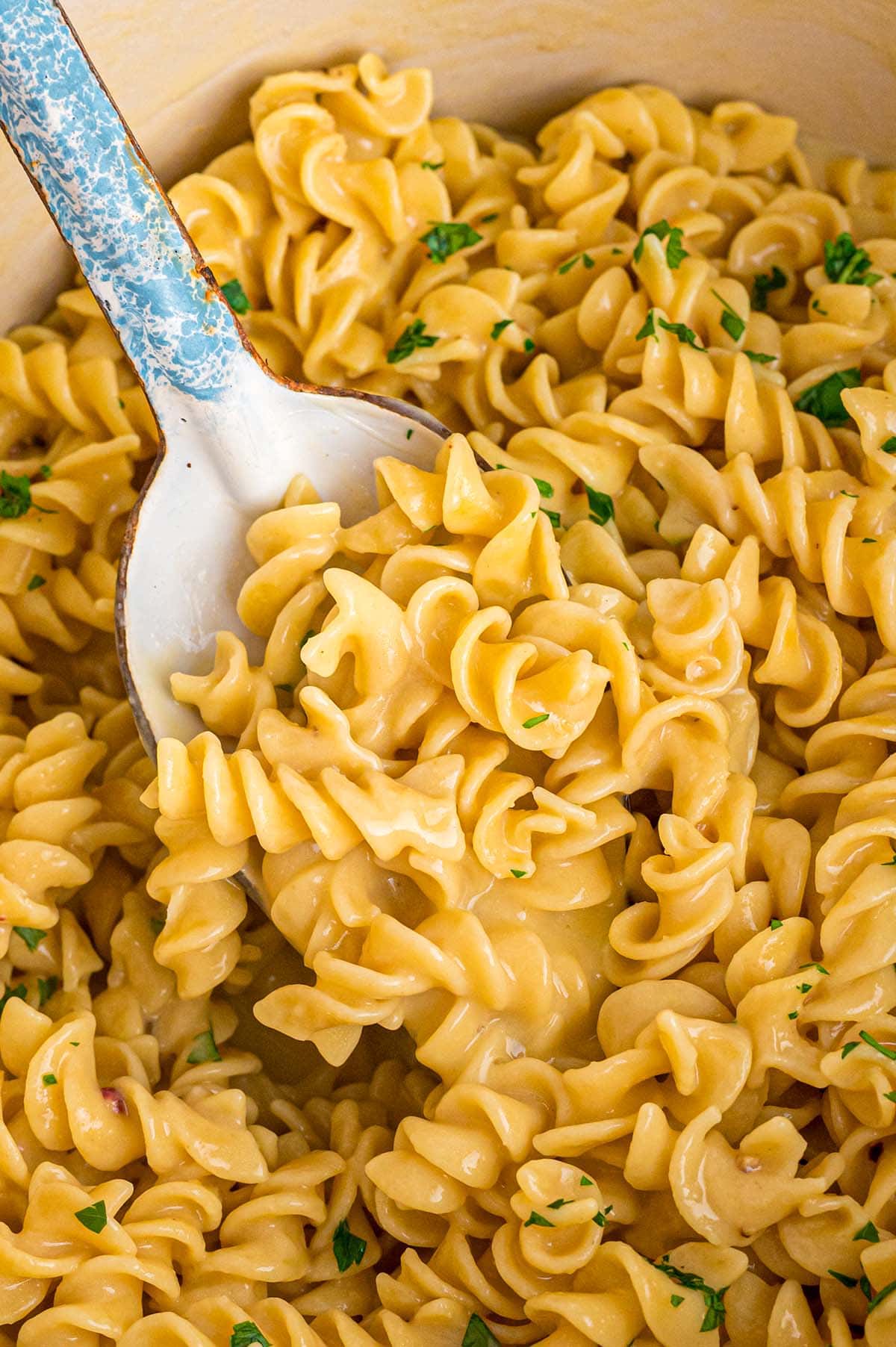 A close-up of simple, cheesy noodles with a spoon ready to serve.