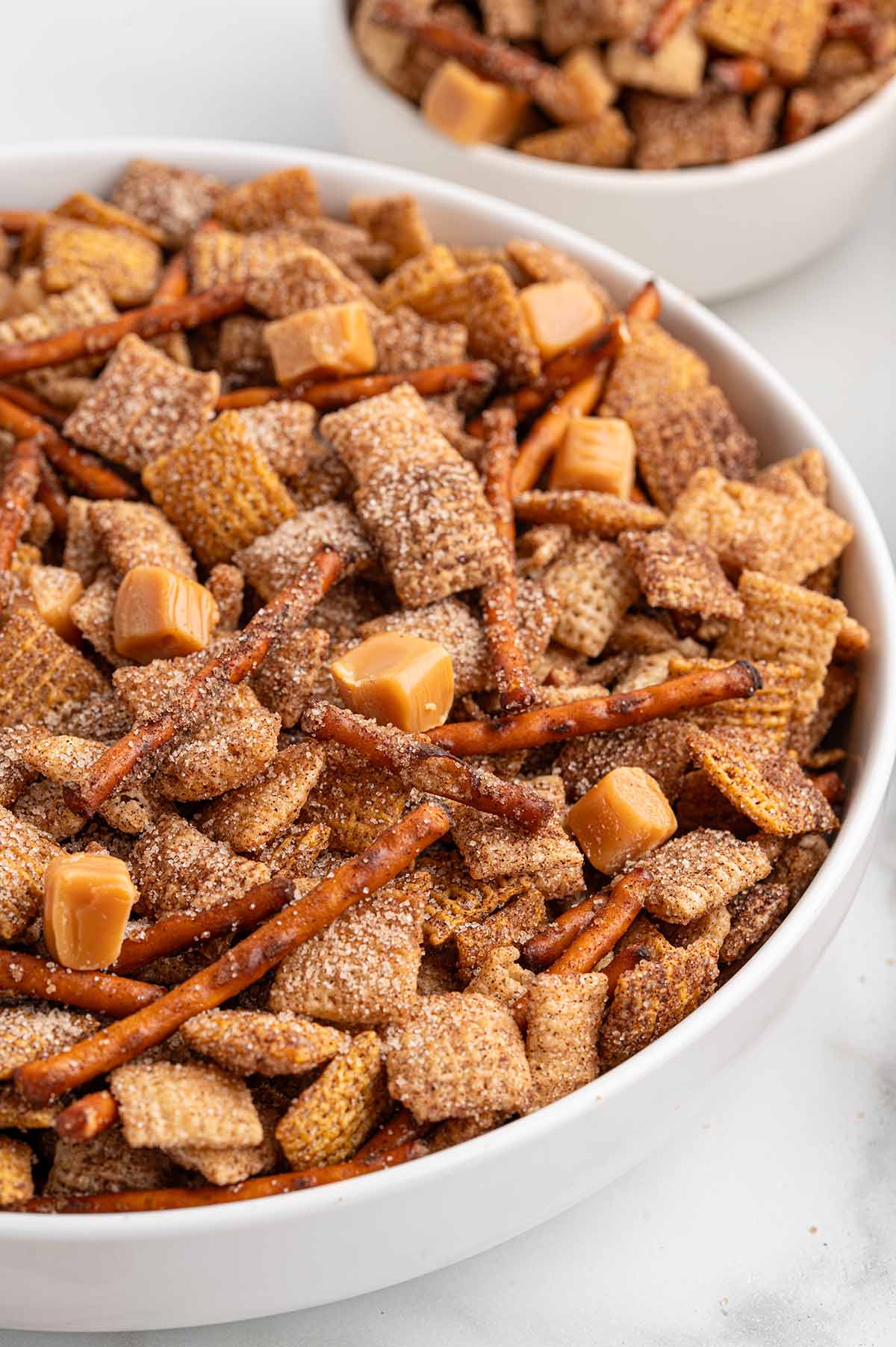 A bowl filled with cinnamon-coated Chex mix, pretzel sticks, and caramel bits.