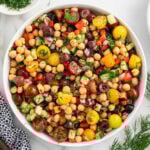 A colorful chickpea salad with cherry tomatoes, olives, cucumber, and fresh herbs in a white bowl.
