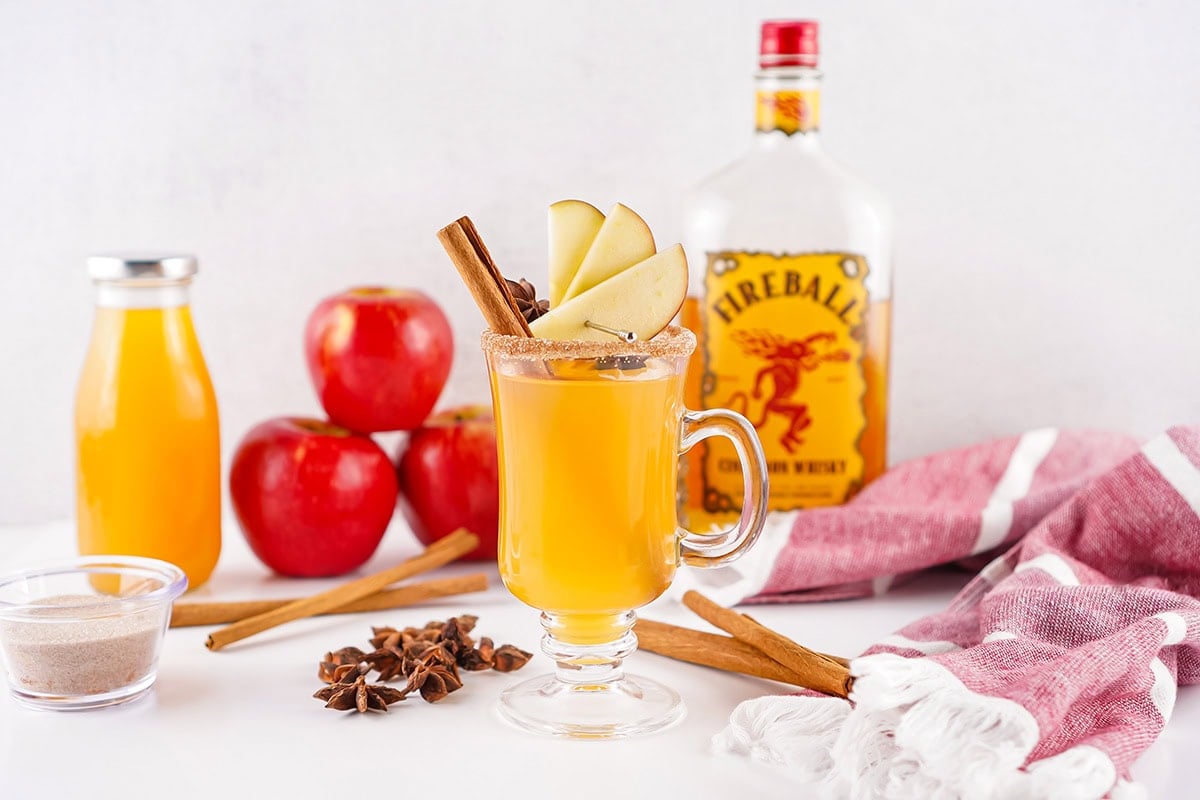 A glass of Fireball Apple Cider garnished with apple slices and a cinnamon stick.