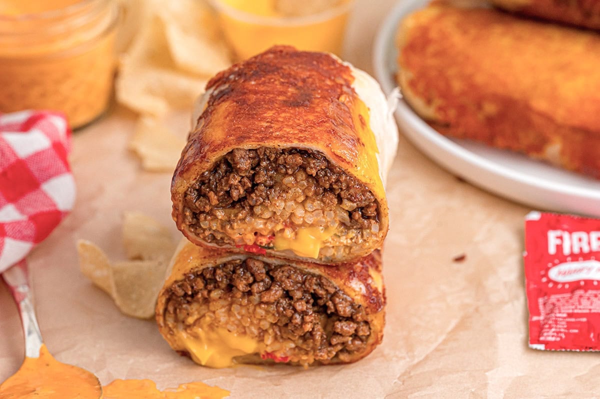 Two halves of a crispy grilled cheese burrito stacked on parchment paper with a sauce packet nearby.
