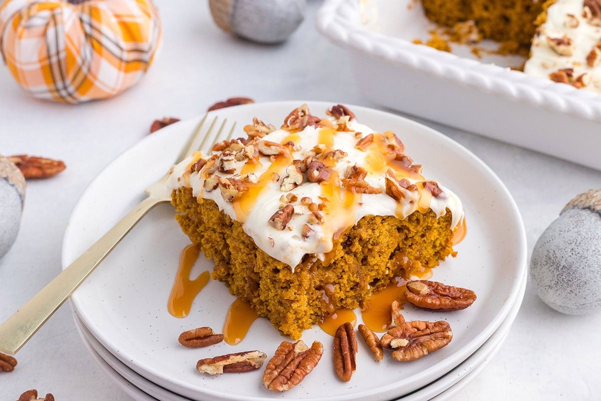 Soft pumpkin cake layered with thick cream and caramel syrup, garnished with pecans.