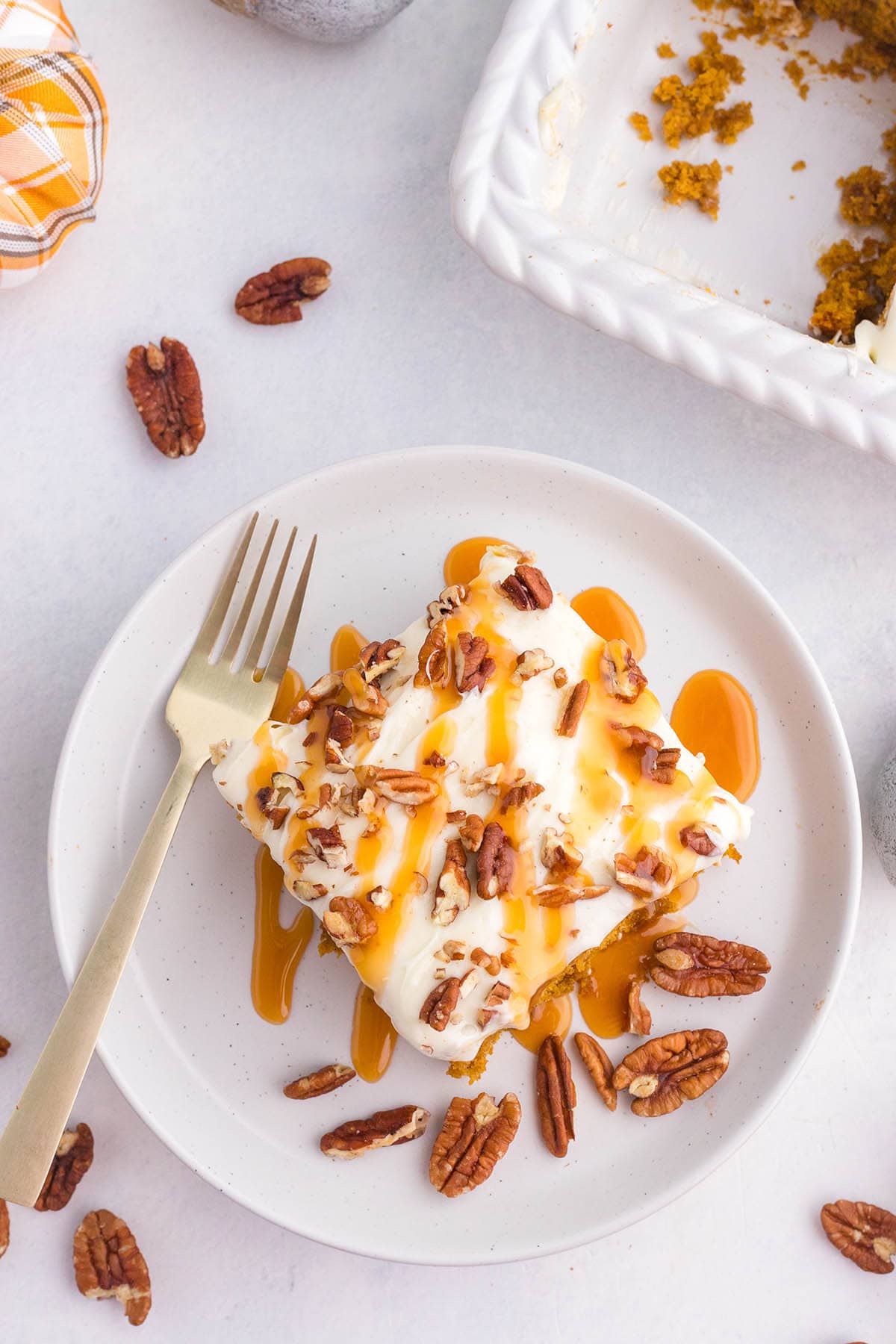 Pumpkin poke cake slice garnished with chopped pecans and drizzled caramel on a simple white plate.