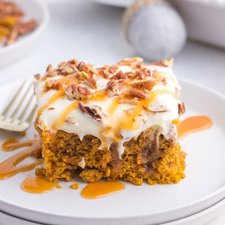 A slice of pumpkin poke cake topped with creamy frosting and chopped pecans.