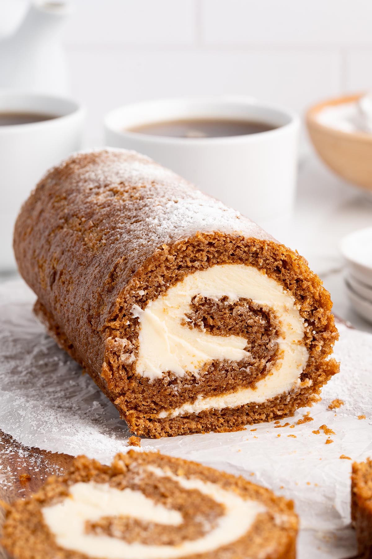 A pumpkin roll cake with creamy filling sits on parchment paper.