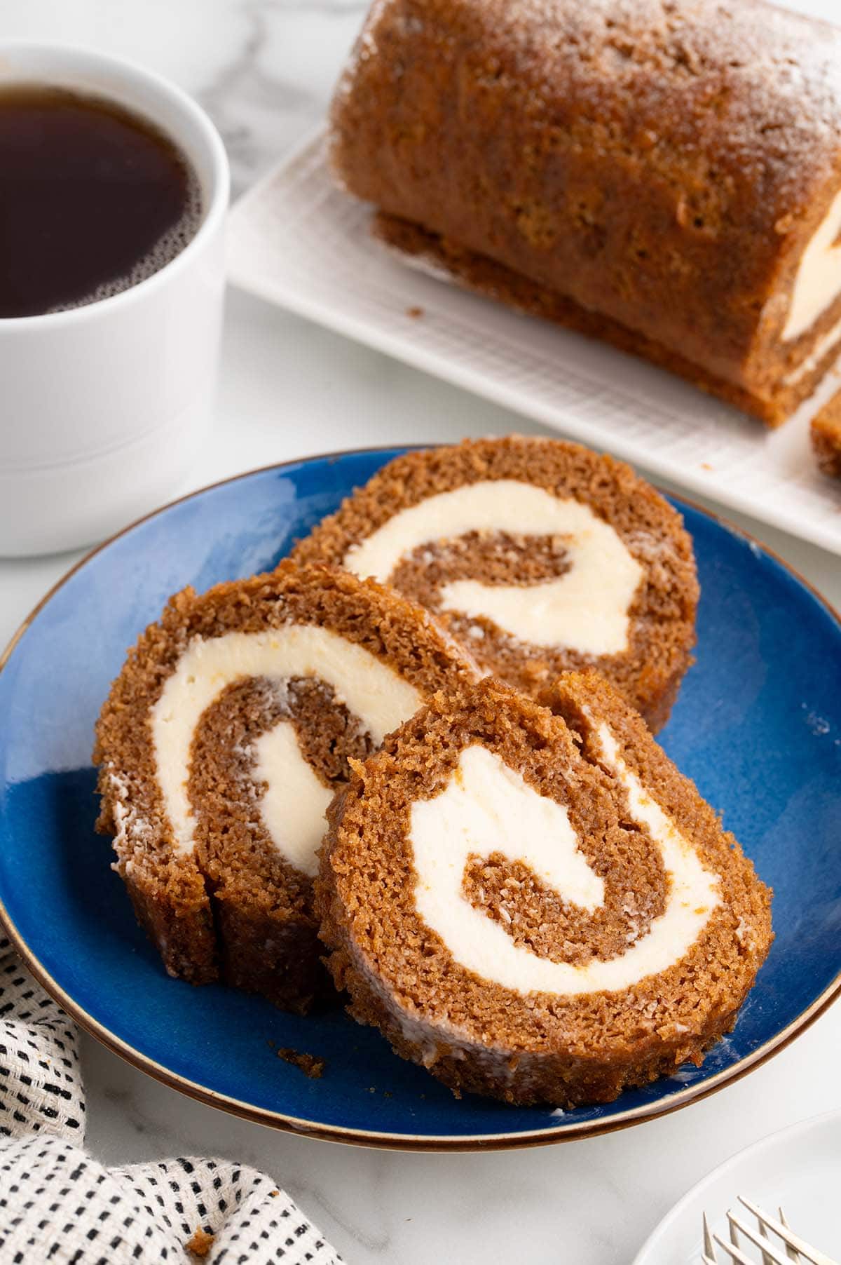 Three slices of pumpkin roll with cream cheese filling on a blue plate.