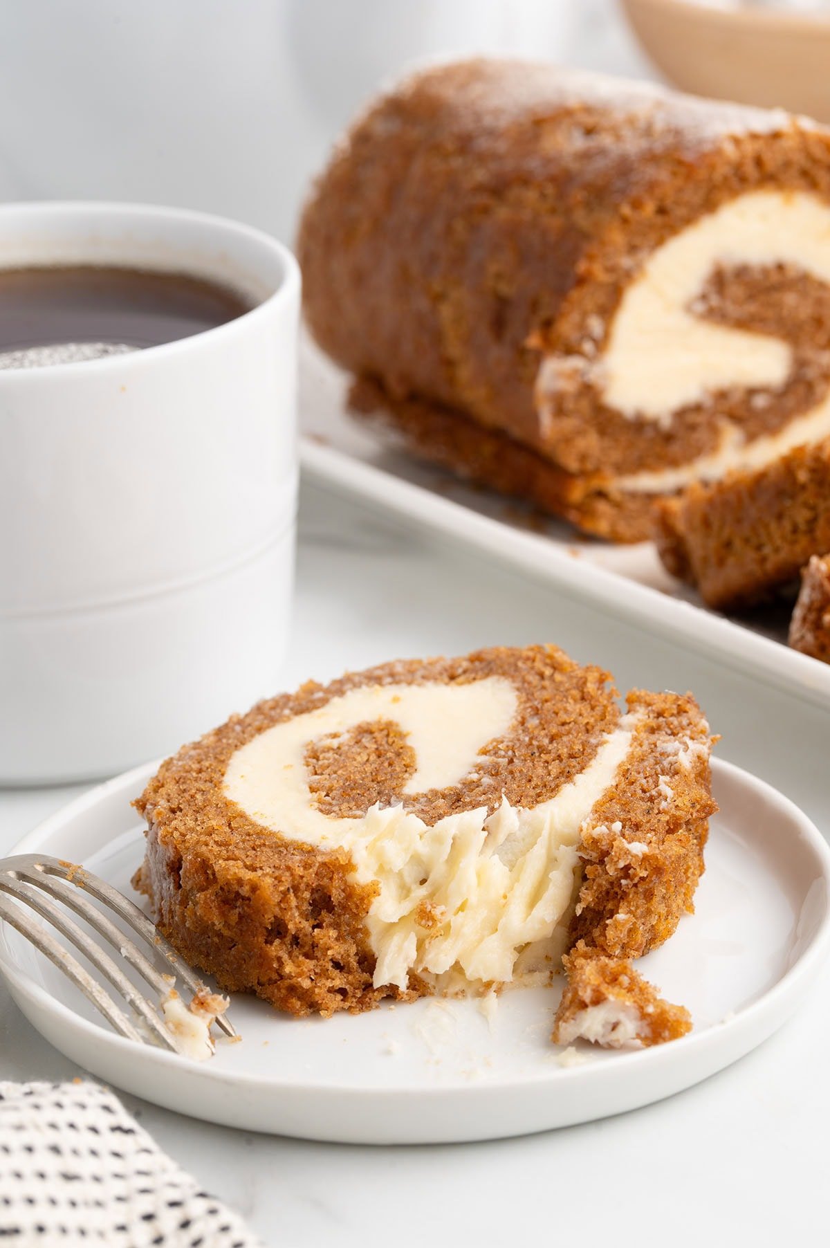 Moist pumpkin roll dessert with a bite taken out on a small plate.