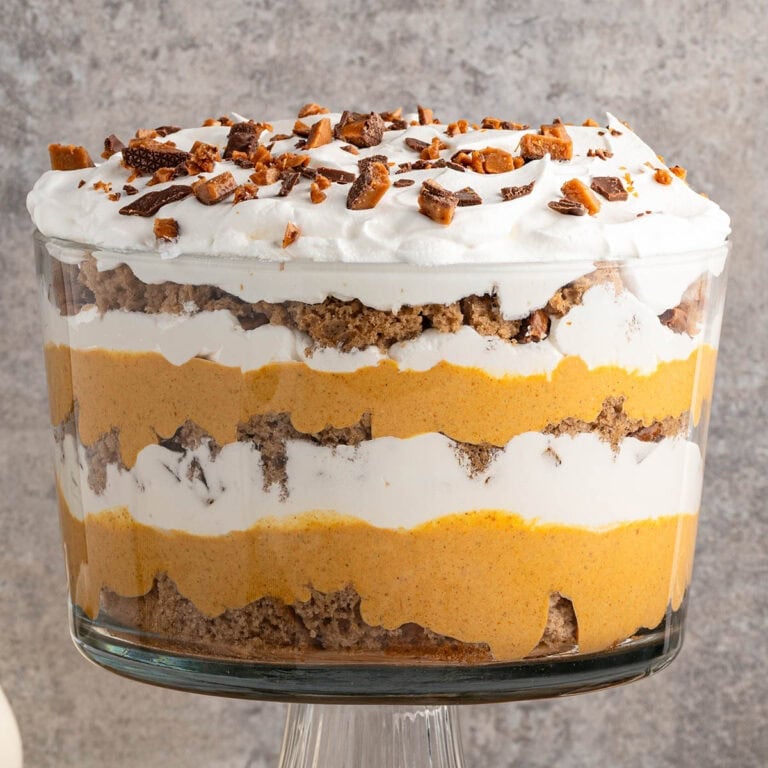 Layered pumpkin trifle in a clear glass bowl with whipped cream and chocolate pieces on top.
