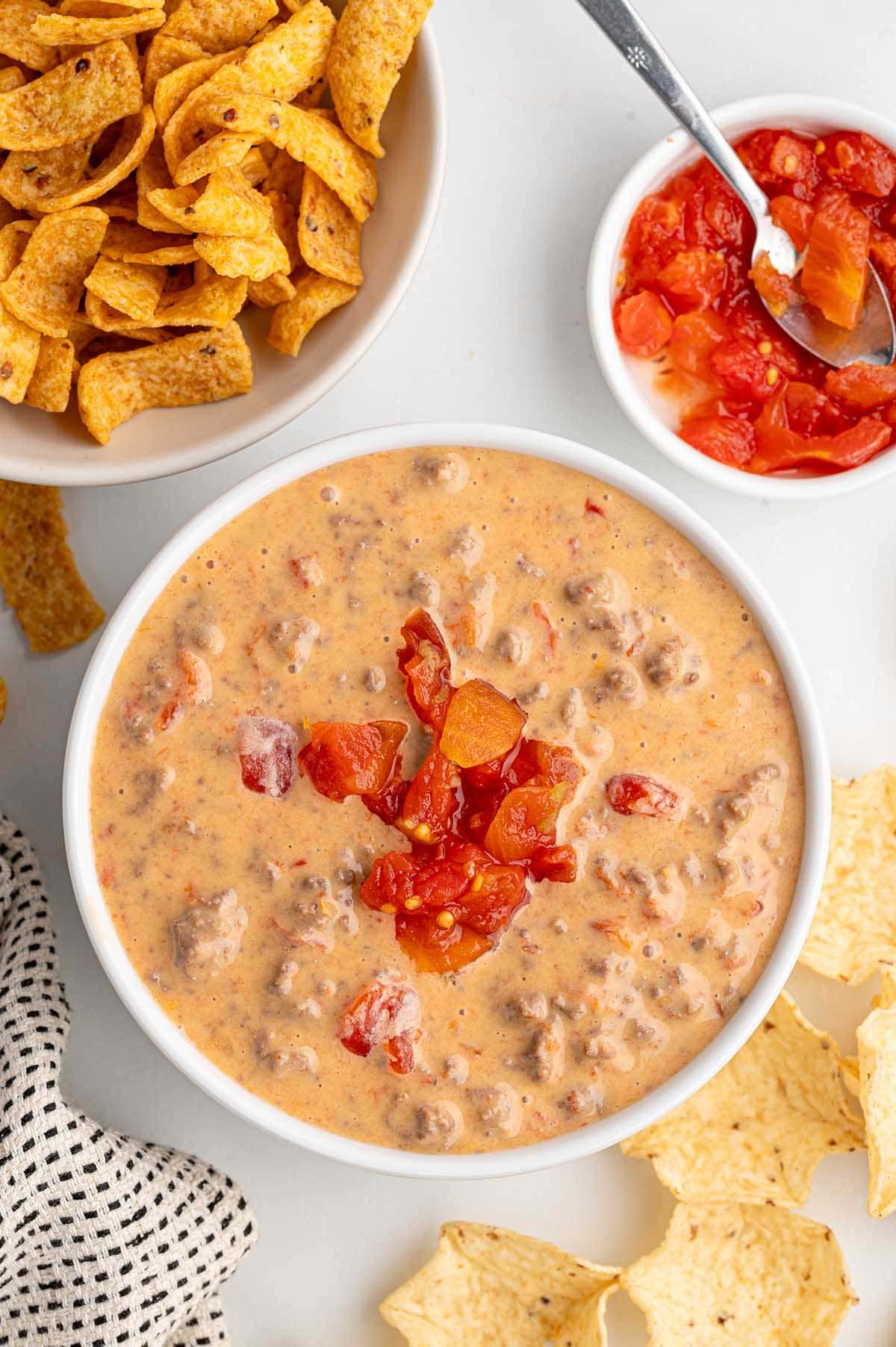 Bowl of creamy Rotel dip topped with diced tomatoes, surrounded by chips and Fritos.