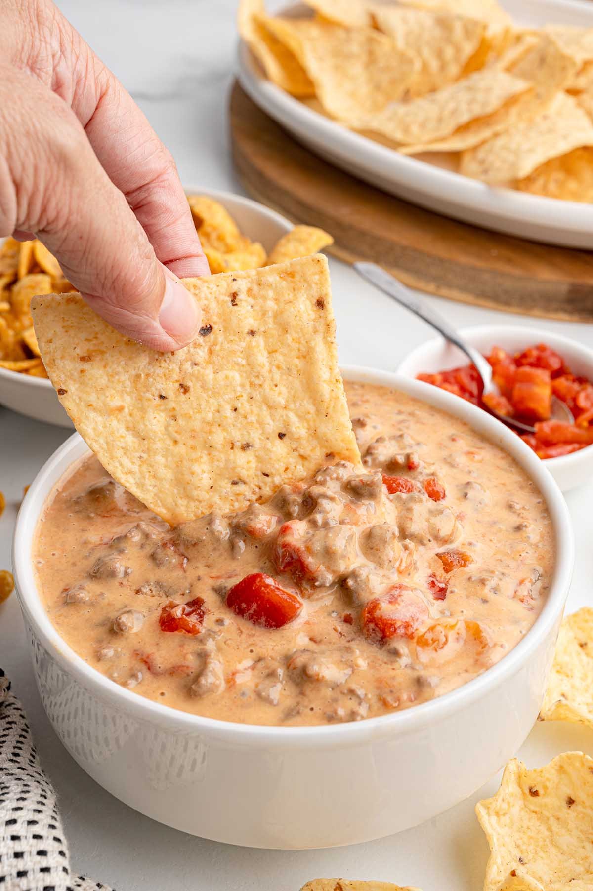 A hand dipping a tortilla chip into a bowl of creamy Rotel dip.