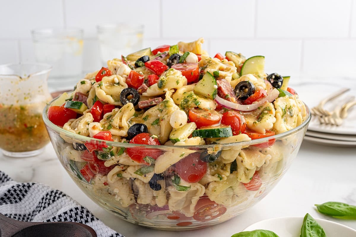 A large bowl of tortellini salad featuring fresh vegetables and herb dressing on a white marble surface.