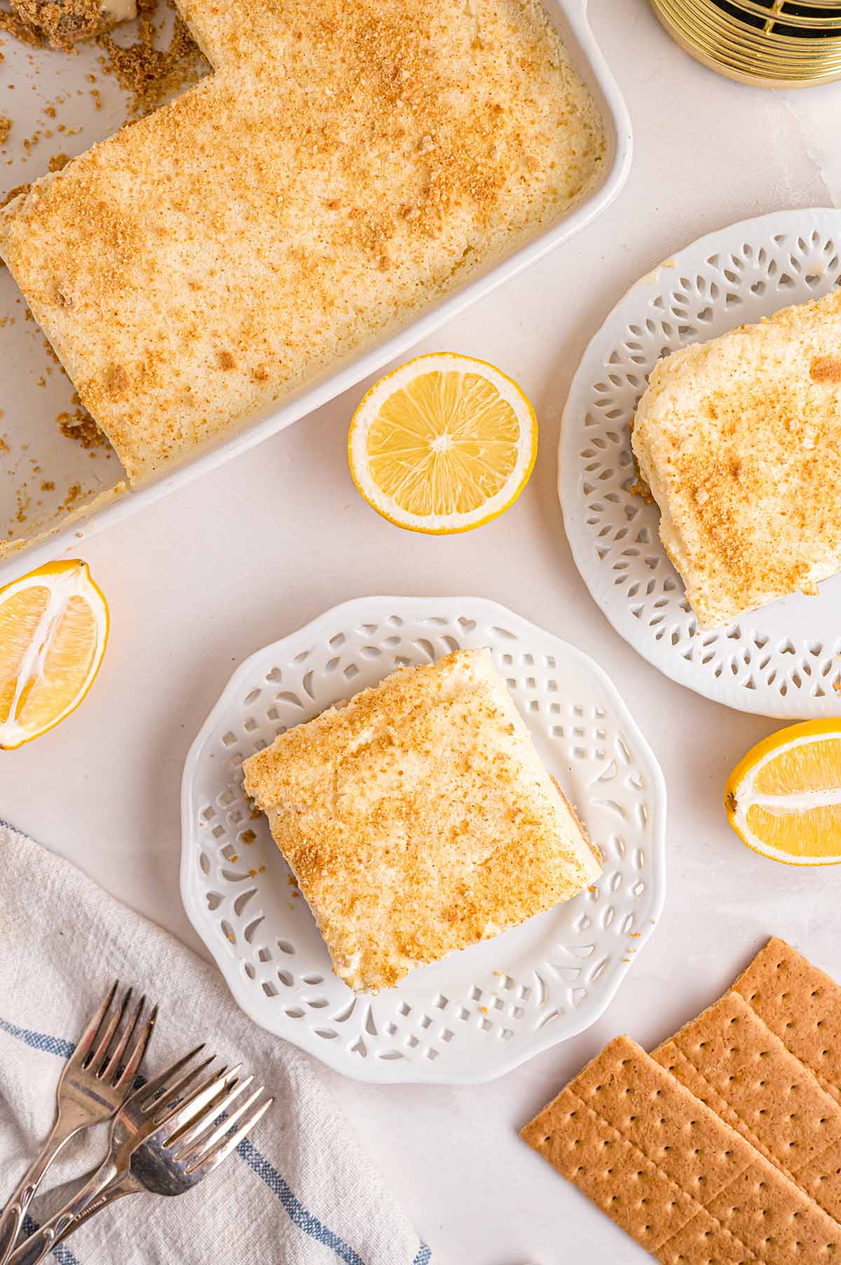 Fresh lemon halves, graham crackers, and two plates of cheesecake on a clean surface.