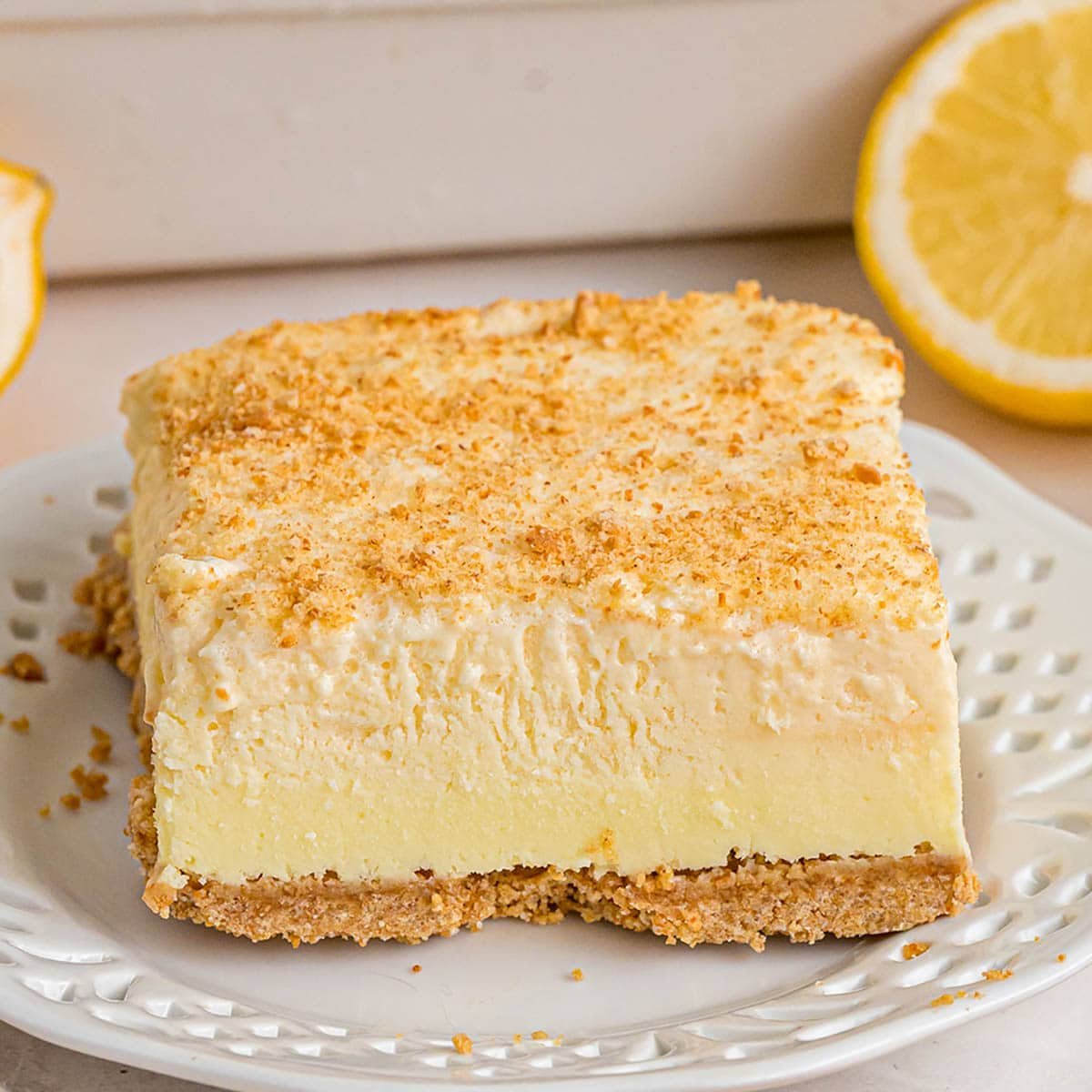 A slice of creamy lemon cheesecake with a crumbly graham cracker crust on a white plate.