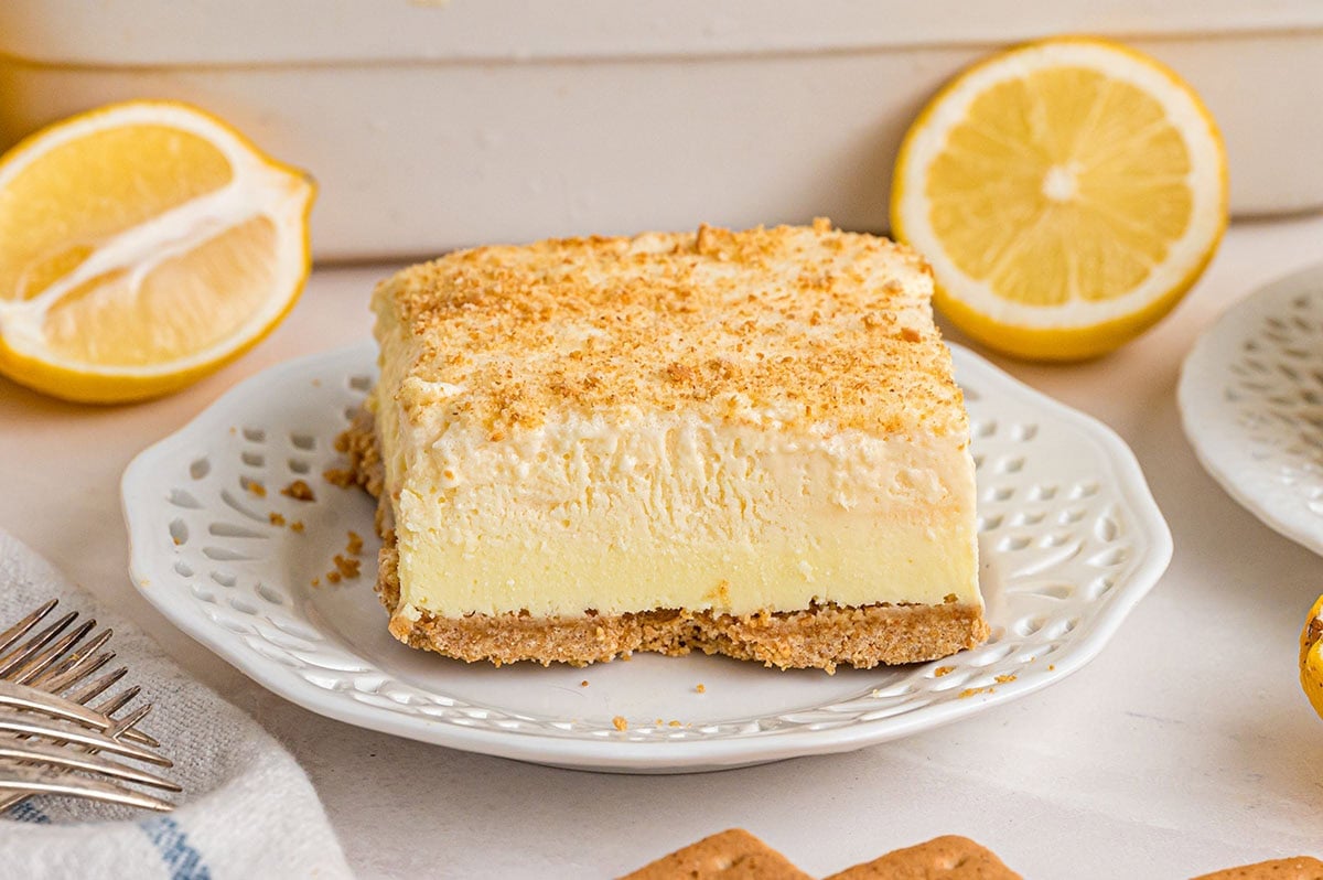 Square lemon cheesecake on a decorative plate, surrounded by fresh lemons.