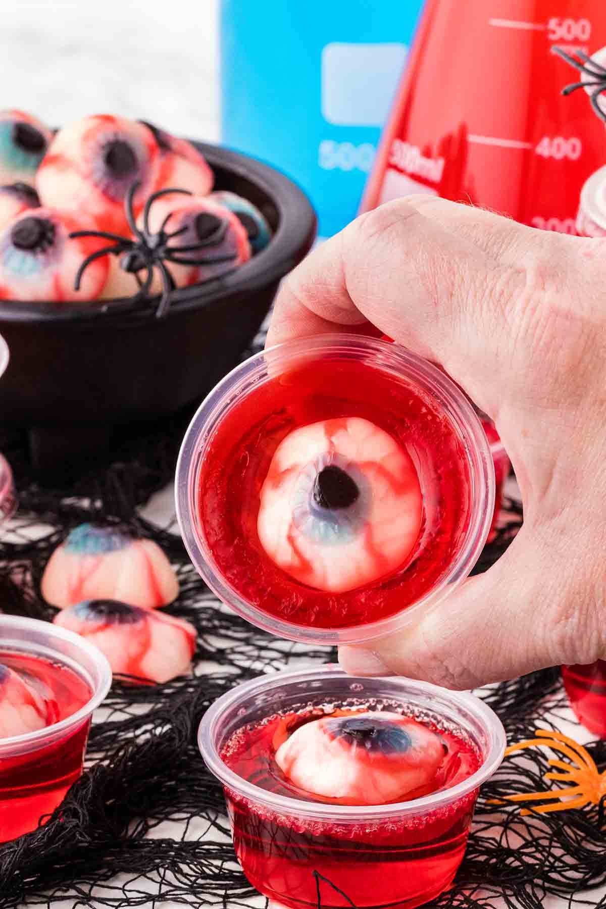 Close-up of red jello shots with realistic eyeball gummies floating inside.