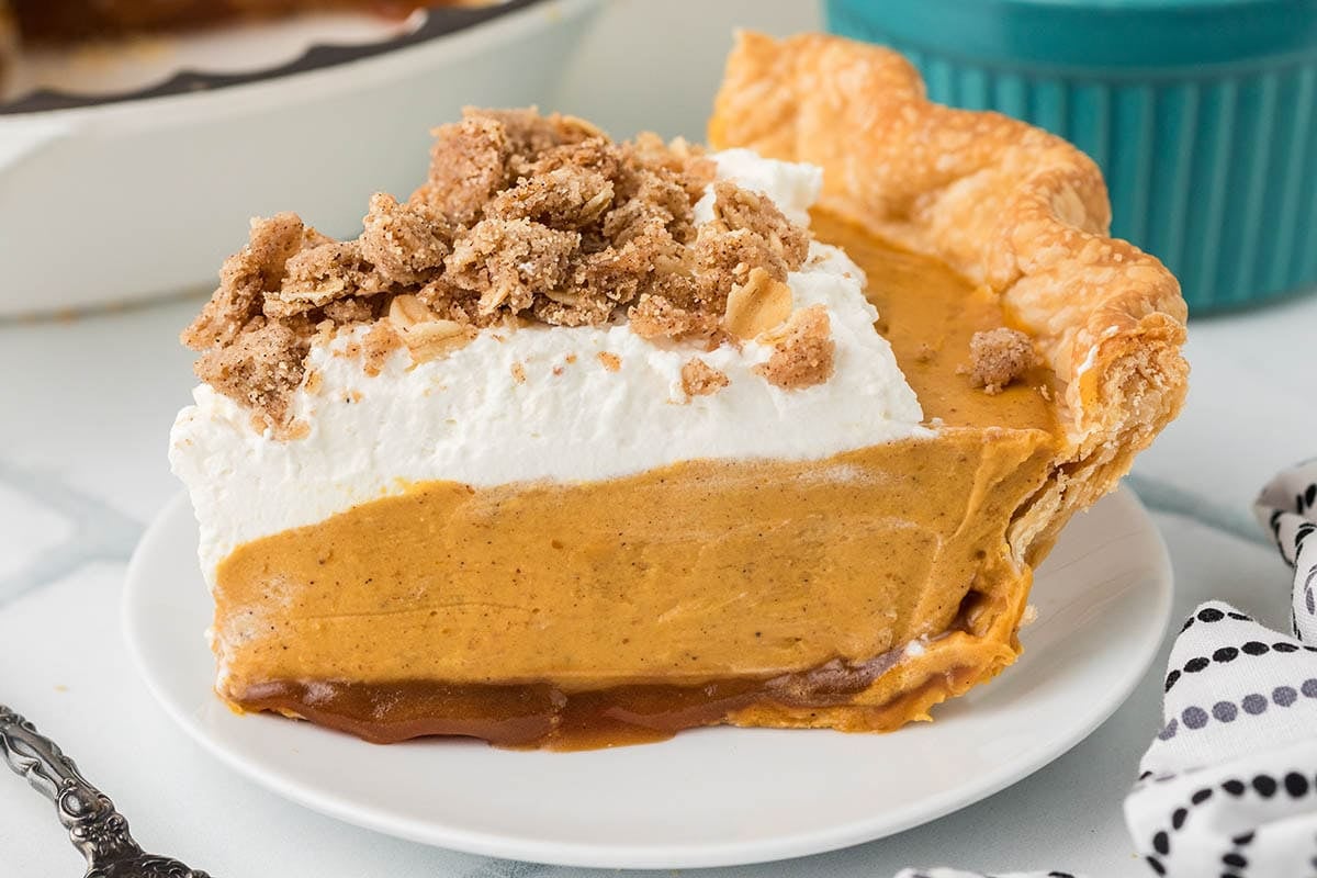 Piece of pumpkin pie with a golden crust and whipped topping on a white dish.