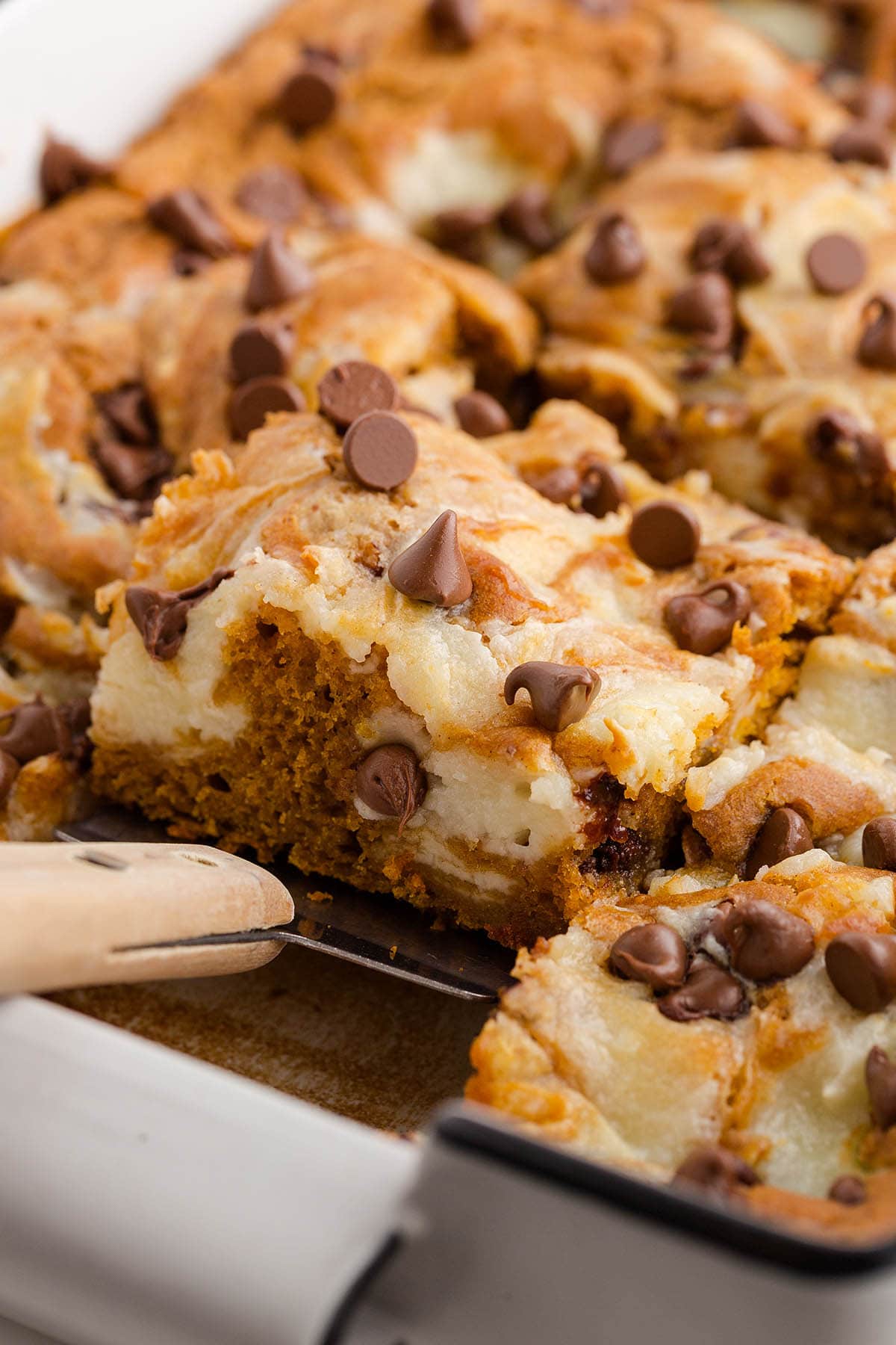 A spatula lifting a slice of pumpkin cake rich in cream cheese and chocolate.