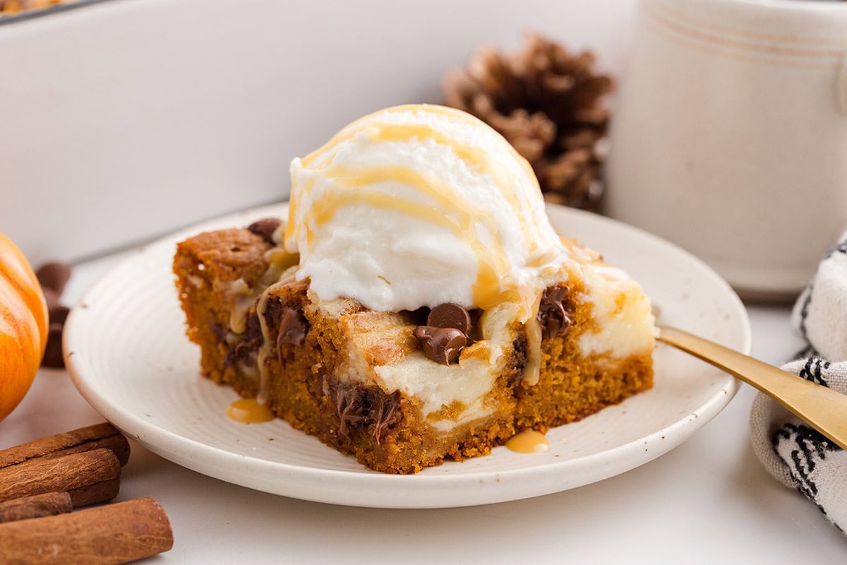 Pumpkin dessert bar with melted chocolate chips and creamy cheesecake, served on a white plate.
