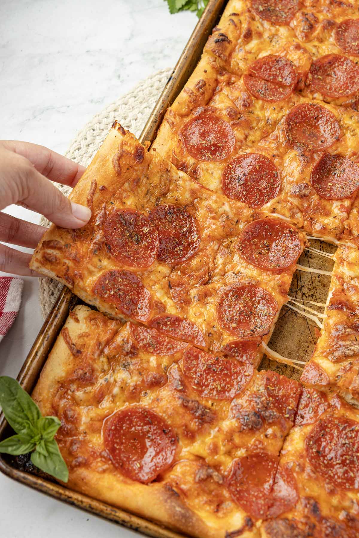 A hand lifts a slice of pepperoni pizza from a sheet pan.