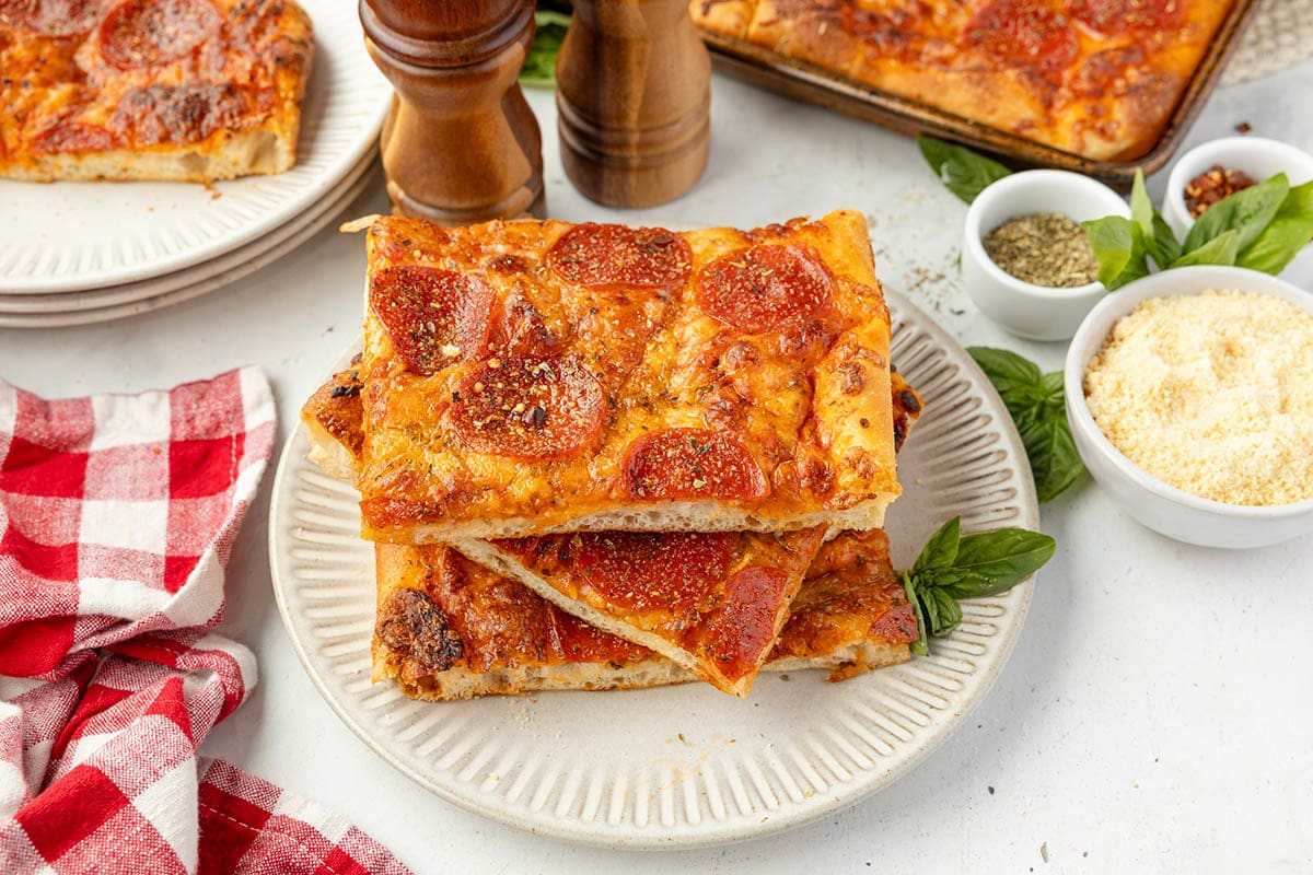 Three slices of pepperoni sheet pan pizza stacked on a white plate.