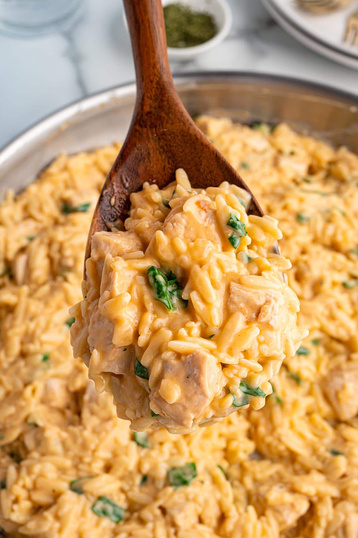 A wooden spoon scooping creamy chicken orzo with spinach from a pot.