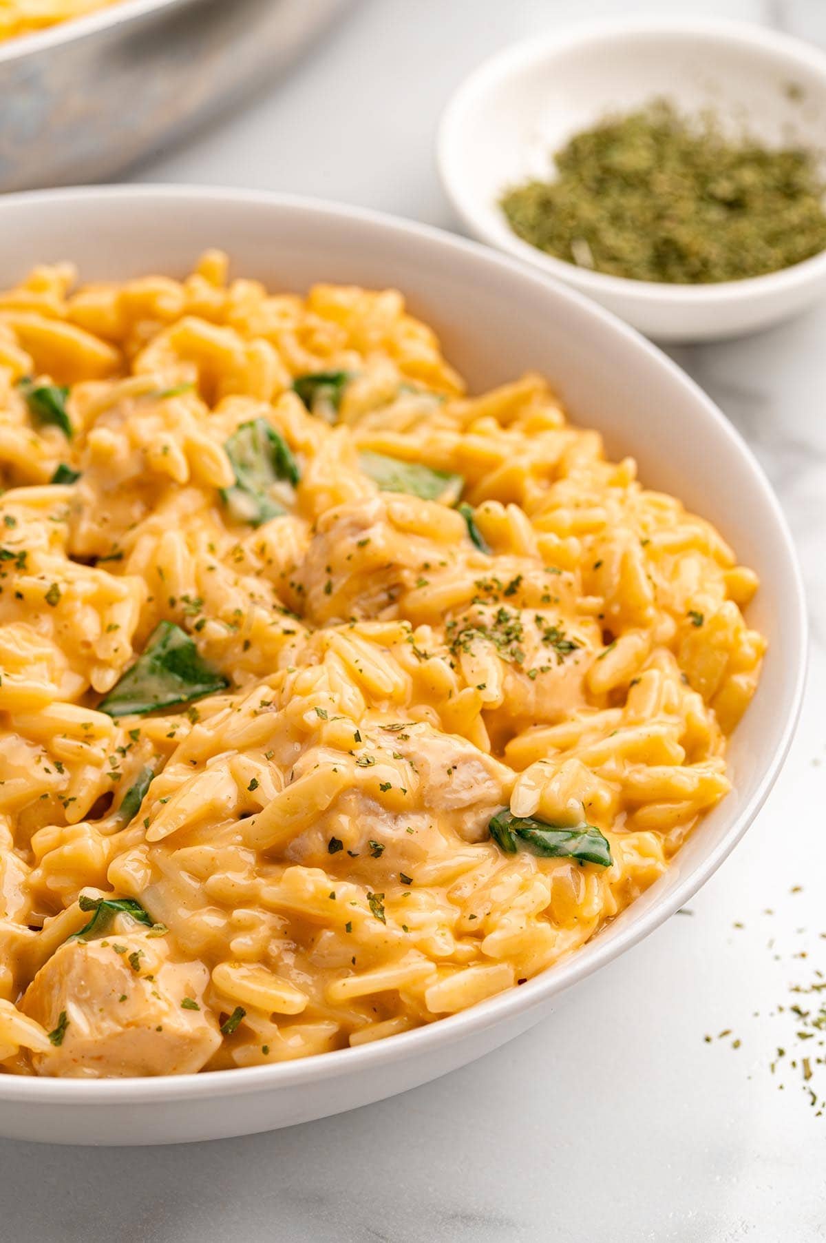 Close up of cheesey chicken orzo on a white plate garnished with dried parsley