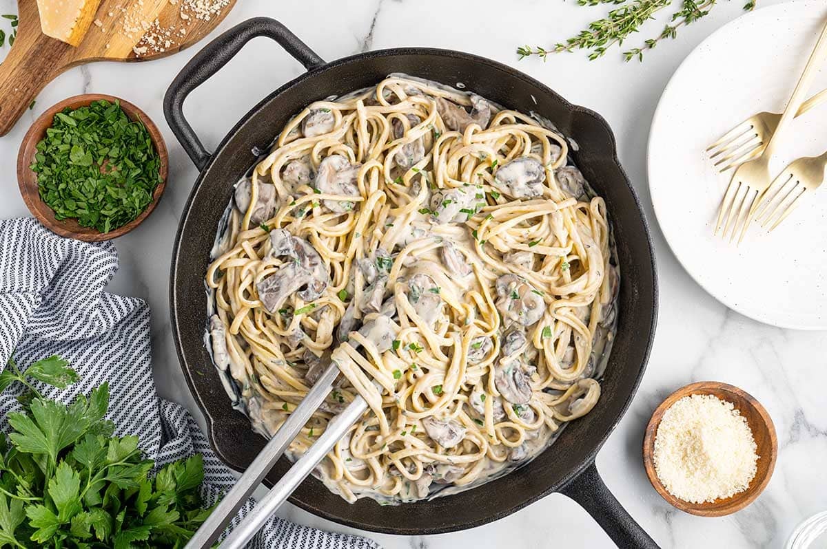 Creamy mushroom pasta in a black skillet, ready to be served with fresh herbs.